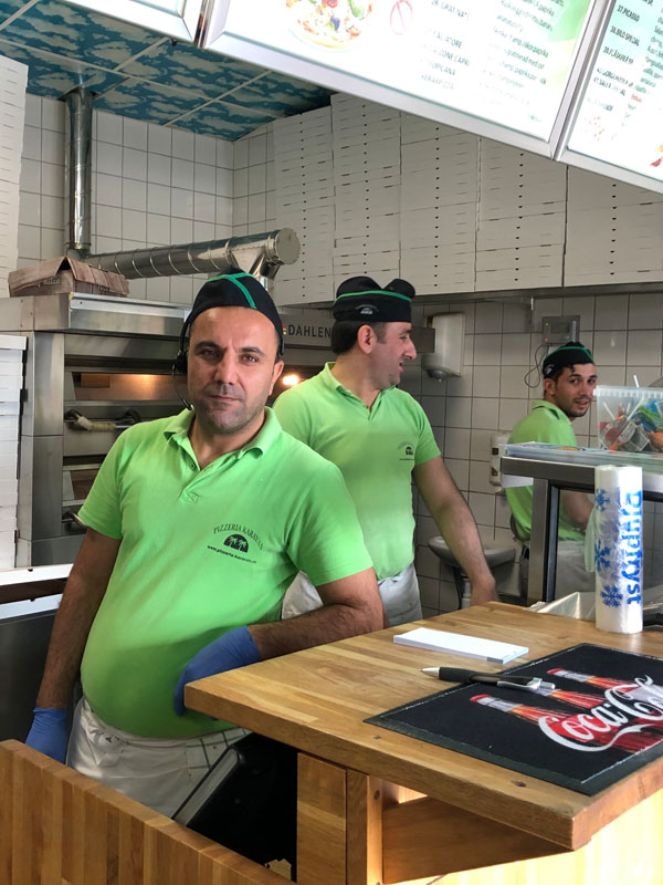 Tre män i gröna tröjor står i ett restaurangkök