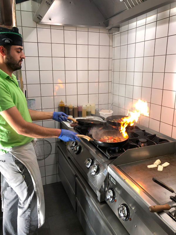 Man i grön tröja lagar mat framför spisen med en stekpanna i handen