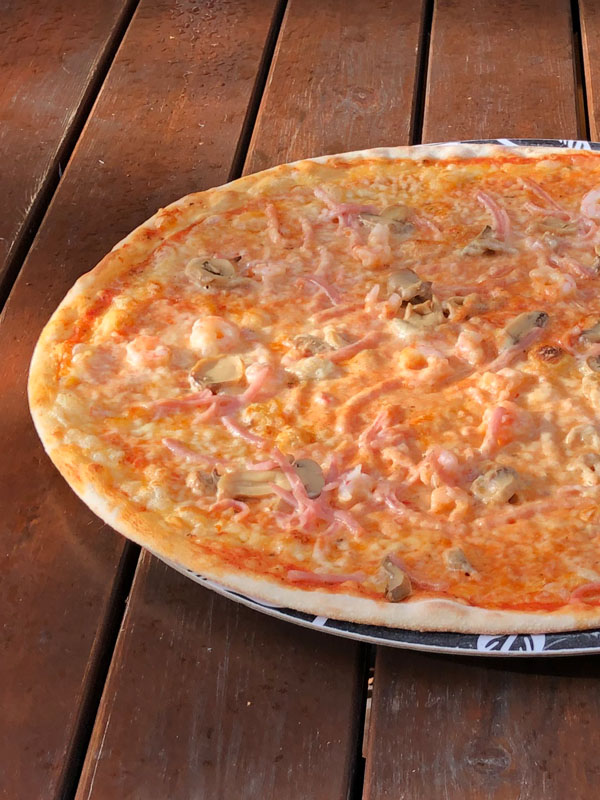 Närbild på en stor pizza toppad med skinka, svamp och räkor